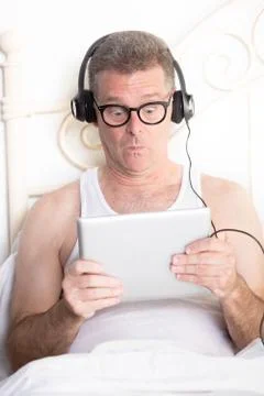 Surprised Man in Bed Looking Down at Computer Tablet Stock Photos