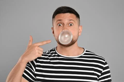 Surprised man blowing bubble gum on light grey background Stock Photos