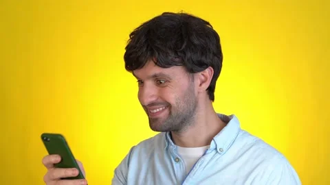 Surprised man isolated on yellow background studio. Using mobile cell phone hold 库存影片 145656231