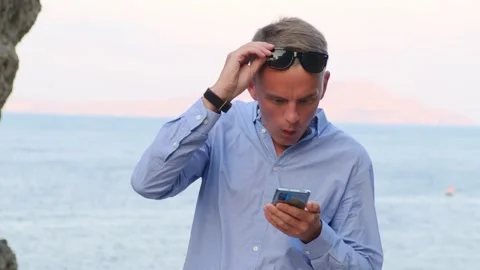Surprised man looking at smartphone screen against the background of the sea Video stock 158673308