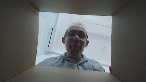 Surprised man opens box, expressing curiosity and excitement as he inspects Vidéo 294896052