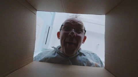 Surprised man opens box, expressing curiosity and excitement as he inspects Stock Footage 294896102