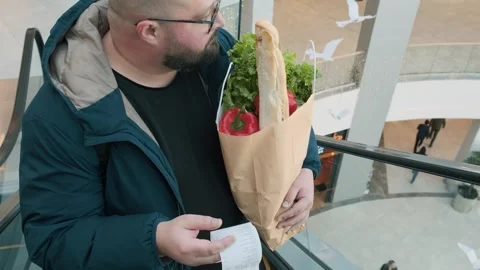 Surprised plus size man with shopping paper bag full of food looks at paper Stock Footage 279647581