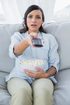 Surprised pretty brunette watching tv and eating pop corn Stock Photos