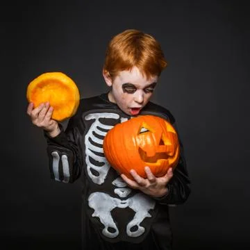Surprised red haired boy in skeleton costume holding a orange pumpkin. Halloween Stock Photos
