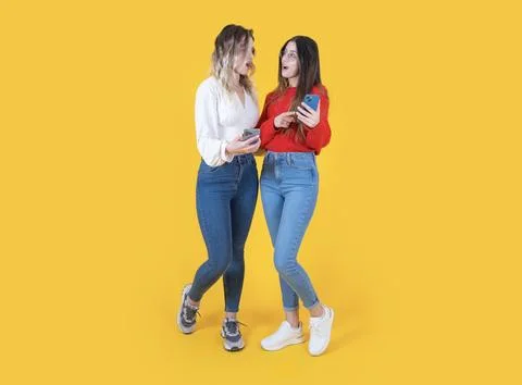 Surprised two full body view woman using phone looking each other Stock Photos