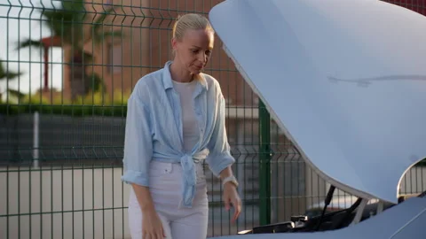 Surprised woman looking under open car hood and feeling confused, trying to.. Stock Footage 337057781