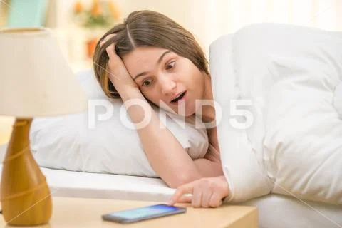 The surprised woman with a phone on the bed Stock Photos