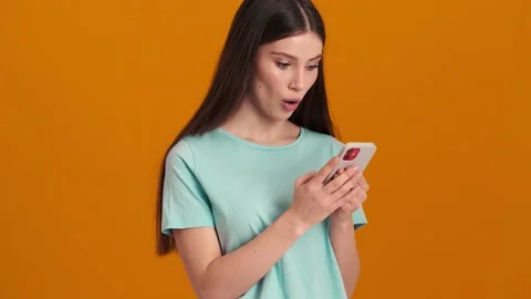 A surprised woman wearing basic T-shirt looking at her smartphone  Stock Footage 154316566