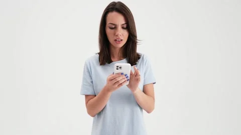 A surprised woman wearing basic t-shirt is using her mobile  스톡 동영상 157867167