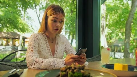 Surprised Young blonde woman using phone sitting in a restaurant. Girl smili Stock Footage 202478199