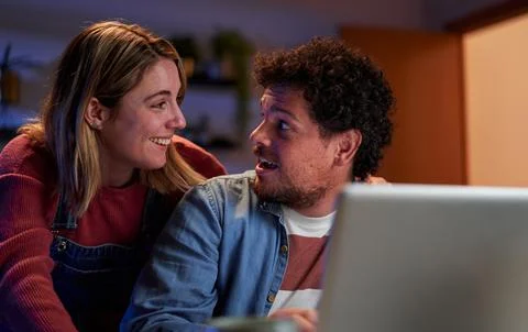 Surprised young couple using a laptop at home at night searching on internet. Stock Photos