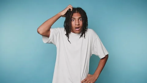 Surprised young man with dreadlocks shows confusion against a blue backgrou.. Stock Footage 313273978
