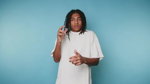 Surprised young man expresses shock while gesturing against a blue background Stock Footage 313273982