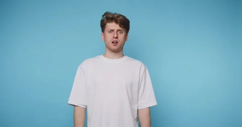 Surprised young man expresses shock in front of a blue background during a .. Stock Footage 316180788