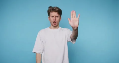 Surprised young man gestures stop something interesting against a blue back.. Stock Footage 316180783