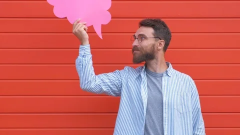 Surprised young man is holding a speech bubble, looking at camera and smiling Stock Footage 111840564