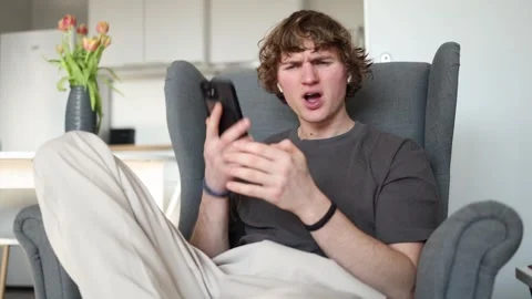 Surprised A young man is looking at his phone with a surprised expression, his e Stock Footage 302634066