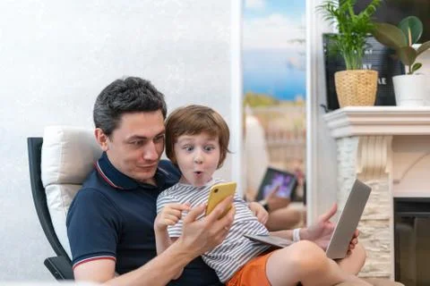 Surprised young man sit on computer using laptop relax with preschooler son h Stock Photos