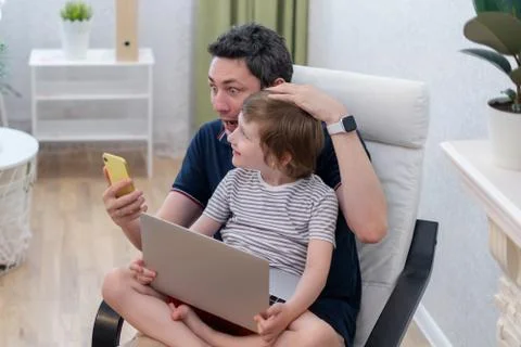 Surprised young man sit on computer using laptop relax with preschooler son h Stock Photos