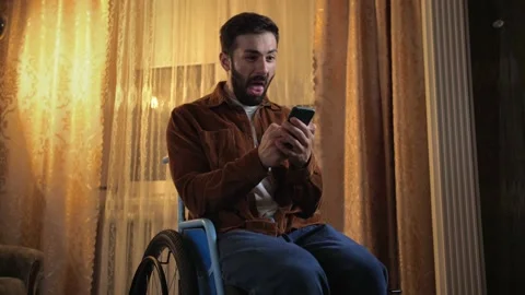 Surprised A young man in a wheelchair is using a phone and screaming into it Stock Footage 202116198