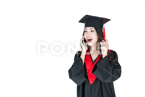 Surprised young woman in mortarboard talking on smartphone and looking away Stock Photos
