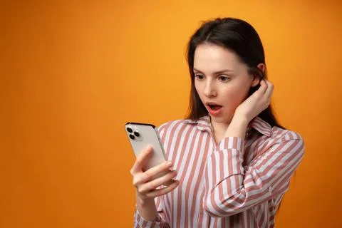 Surprised young woman using smartphone against yellow background Stock Photos
