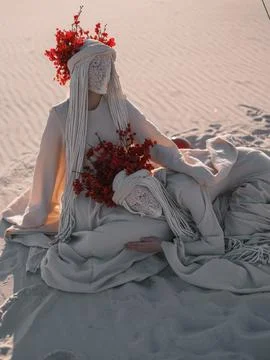 Surreal performance art two figures resting white costumes red flowers sand.. Foto stock