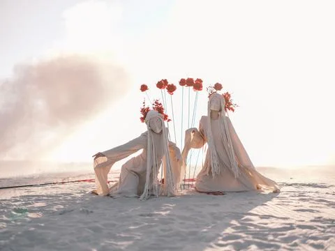 Surreal performance art two figures white costumes red flowers sand dunes smo Foto stock