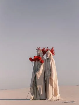 Surreal performance art two figures white costumes red flowers desert Foto stock