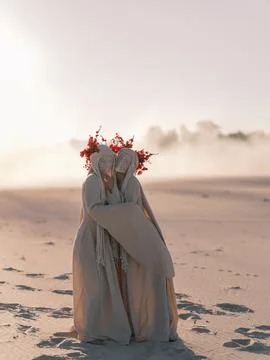 Surreal performance art two figures white costumes red flowers hugging dese.. Foto stock