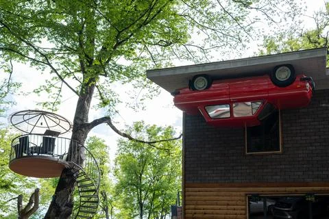 Surreal Upside Down Red Car Attached to Forest Building. 库存照片