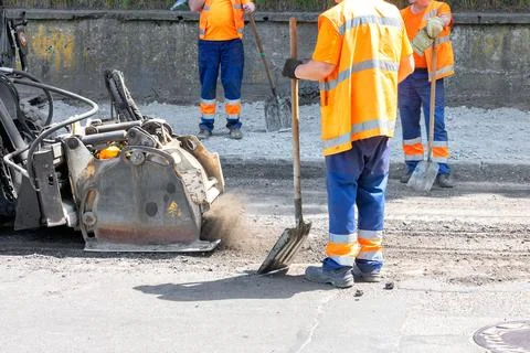 Surrounded by a team of road workers in orange overalls, an industrial millin Stock Photos