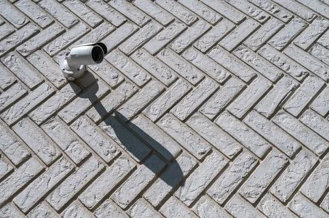 Surveillance camera casting sharp shadow on brick wall in sunlight Stock Photos