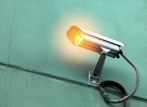 Surveillance camera with warning light mounted on green wall Stock Photos