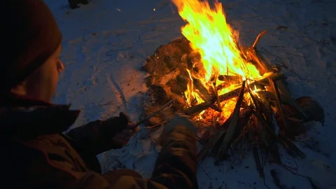 Survival master planes a stick while sitting by the fire at night Stock Footage 121133917