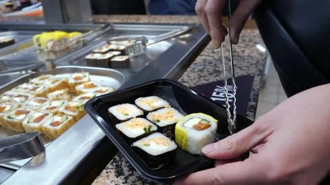 Sushi bar. Buffet table Women's hands put fresh sushi in a container Stock Footage 297210713