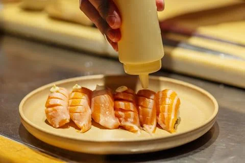 Sushi chef adding sauce to freshly prepared salmon sushi on plate Stock Photos