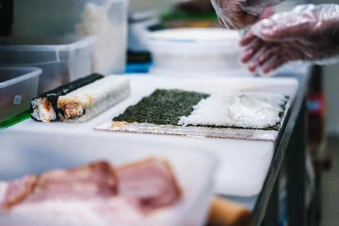 Sushi maker prepares rolls puts rice on a sheet of nori Stock Photos