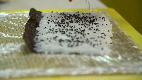 Sushi making process, pouring black seeds on the rice in the nori leaves, 4k Stock Footage 129323285