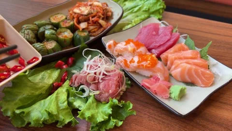 Sushi platter with vibrant rolls, sashimi, and garnishes on a wooden table in a Stock Footage 320408698