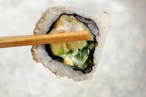 Sushi roll held with chopsticks in a dining setting Stock Photos