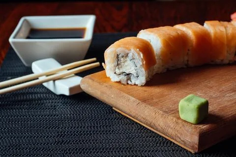 A sushi roll with a piece missing sits on a wooden board Stock Photos