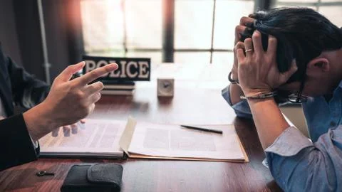 Suspect with handcuffs being interviewed in interrogation room by Police offi Stock Photos