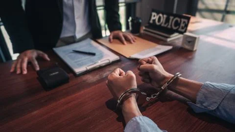 Suspect with handcuffs being interviewed in interrogation room by Police offi Stock Photos
