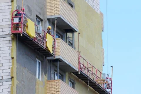 Suspended cradle for worker for facing facade of tall building under construc Stock Photos