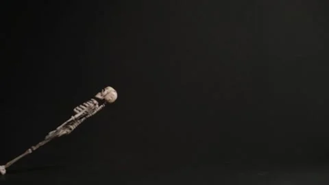 The suspended skeleton is dragged from left to right on black background. Slowmo Stock Footage 160521227