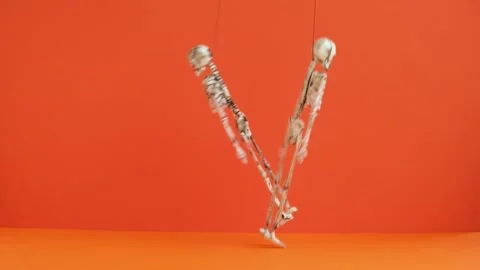 Suspended skeletons dance on a orange background. Preparing for Halloween party. Stock Footage 160940534