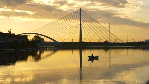 Suspension bridge over the river at sunset and a fisherman in a boat. Stock Footage 156132357
