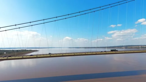 Suspension bridge spans wide river under clear blue sky Stock Footage 343525059